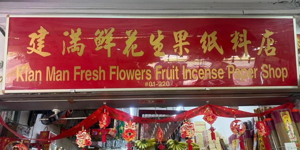 Shop signboard for Kian Man Fresh Flowers Fruit Incense Paper Shop with vibrant red and gold colors.