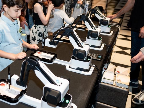 Children and adults engaging with robotic arms at an event.