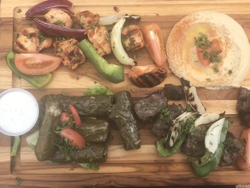 A board of grilled chicken, vegetables, hummus and stuffed grape leaves