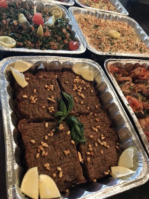 A catering tray of baked kibbeh with lemon wedges