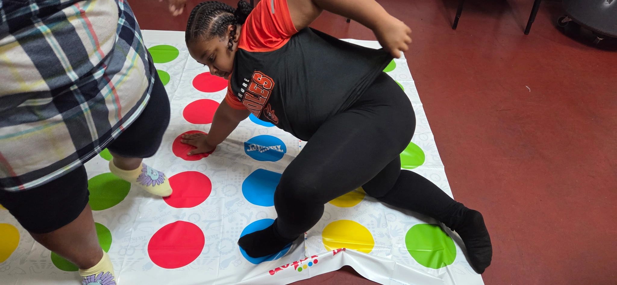 Two people playing Twister on a mat with colorful circles.