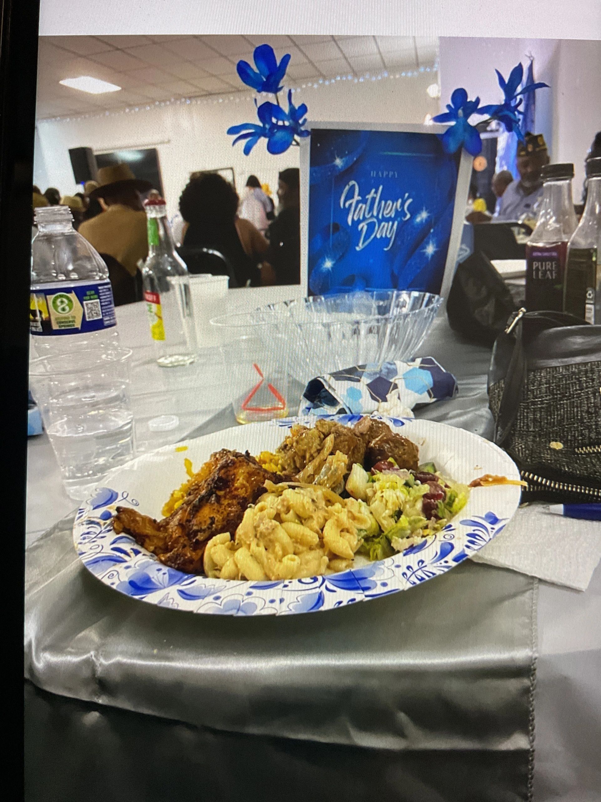 Plate of food at a Father's Day event with decorations and people in the background.