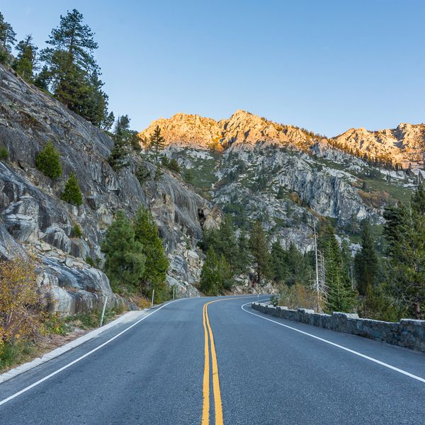 Empty road winding through rocky mountains at sunset.