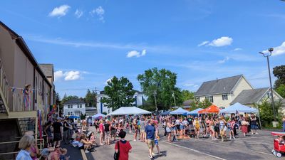 Community outdoor event with people gathered under tents on a sunny day.