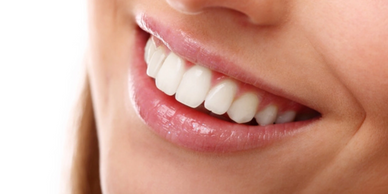 Close-up of a smiling mouth with white teeth and pink lips.