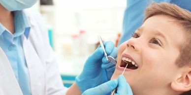 A child smiling during a dental checkup by a masked dentist.