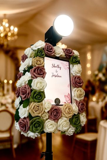 A photo booth decorated with colorful artificial roses for a wedding event.