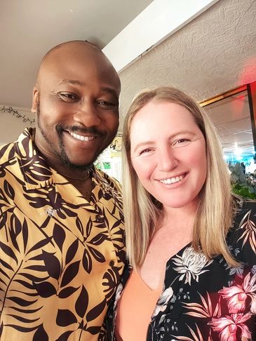 A smiling couple wearing floral shirts posing indoors for a selfie.