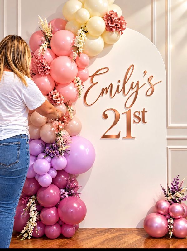 Bespoke pink, lilac and cream birthday balloon arch being styled with floral decorations and a perso