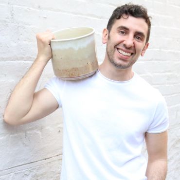 Man smiling, holding large ceramic mug on shoulder.