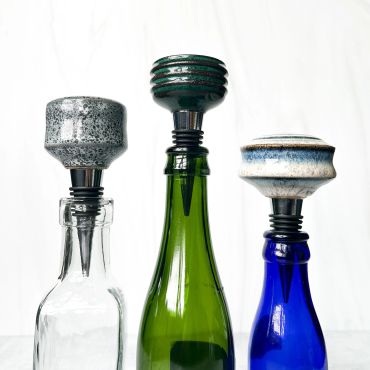Three uniquely designed bottle stoppers on glass bottles.