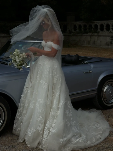 Bride in elegant off-shoulder gown with veil and bouquet.