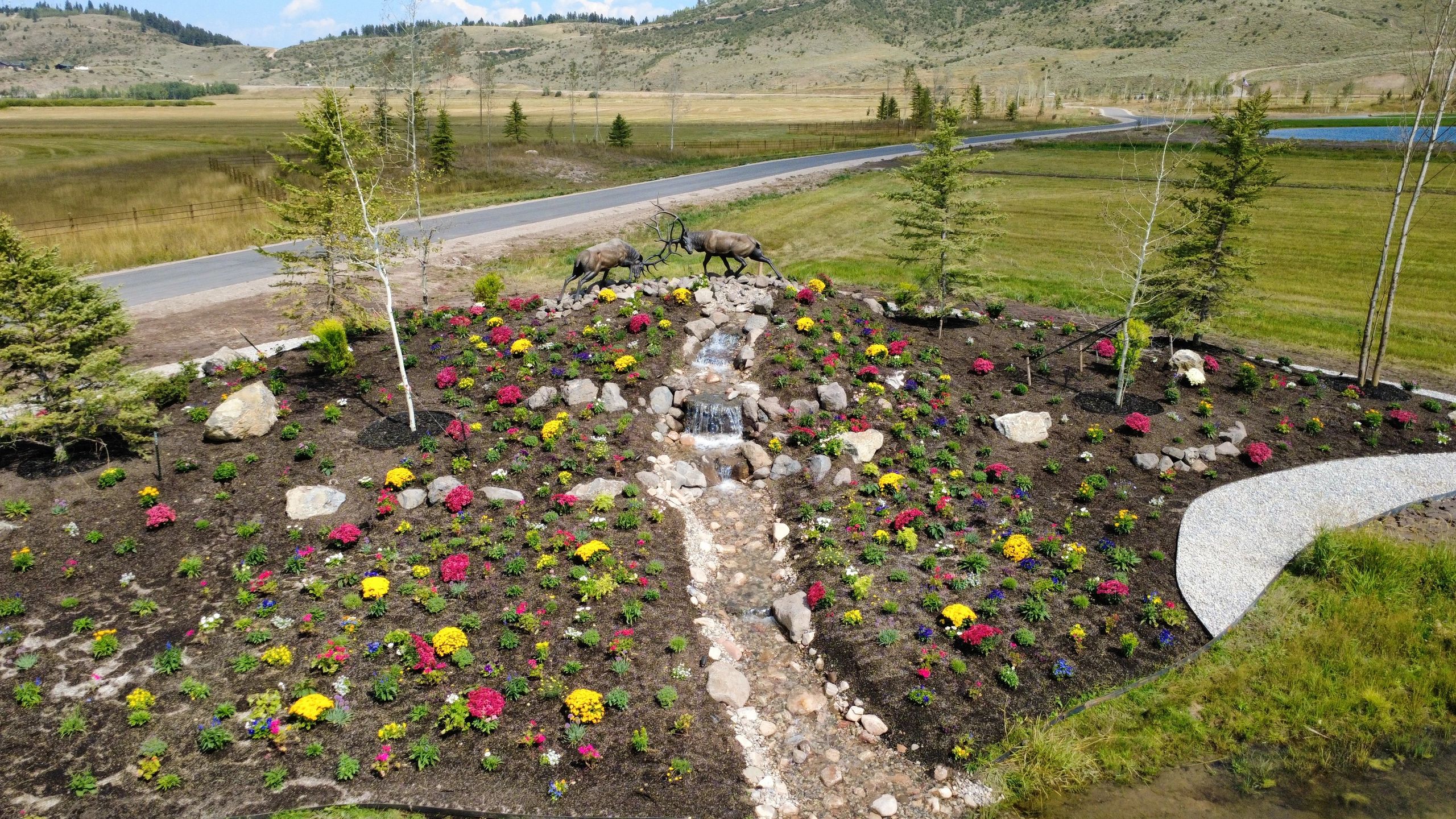 Landscape installation with colorful flower beds, rock, trees, and water feature in Star Valley, Wyoming.