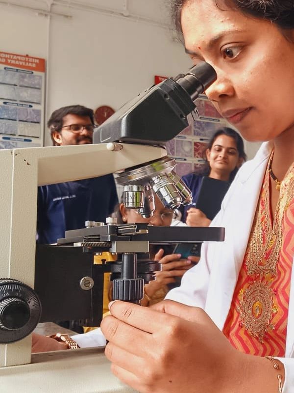 A woman closely observing a sample through a microscope in a lab setting.
