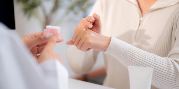 Person applying cream on their hand from a jar.