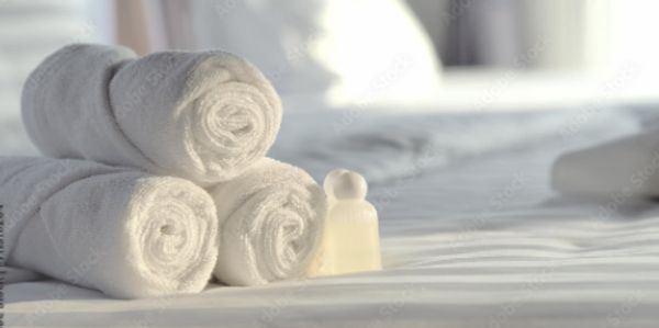 Rolled white towels and a small soap on a bed.