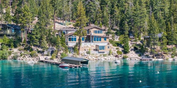 Lakefront houses surrounded by trees and clear blue water.