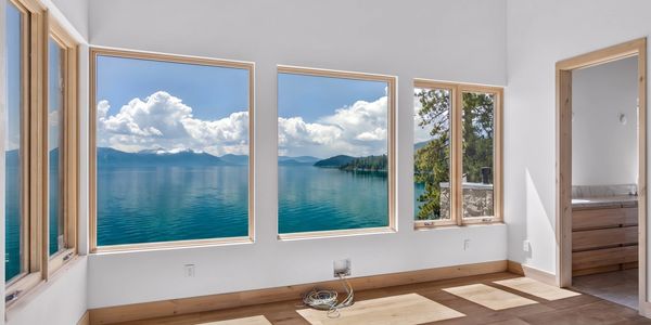 Room with large windows showing a scenic lake and mountain view.