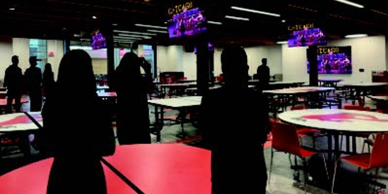 Silhouetted people in a dimly lit room with tables and screens.