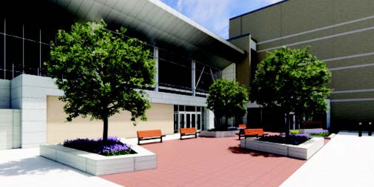Modern outdoor plaza with trees, benches, and a building entrance.