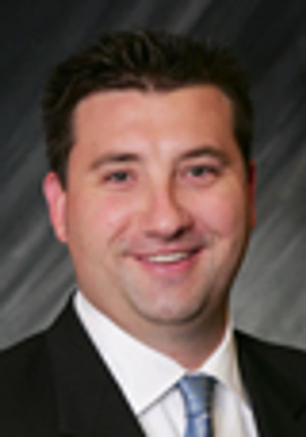 A man in a suit smiling against a dark background.