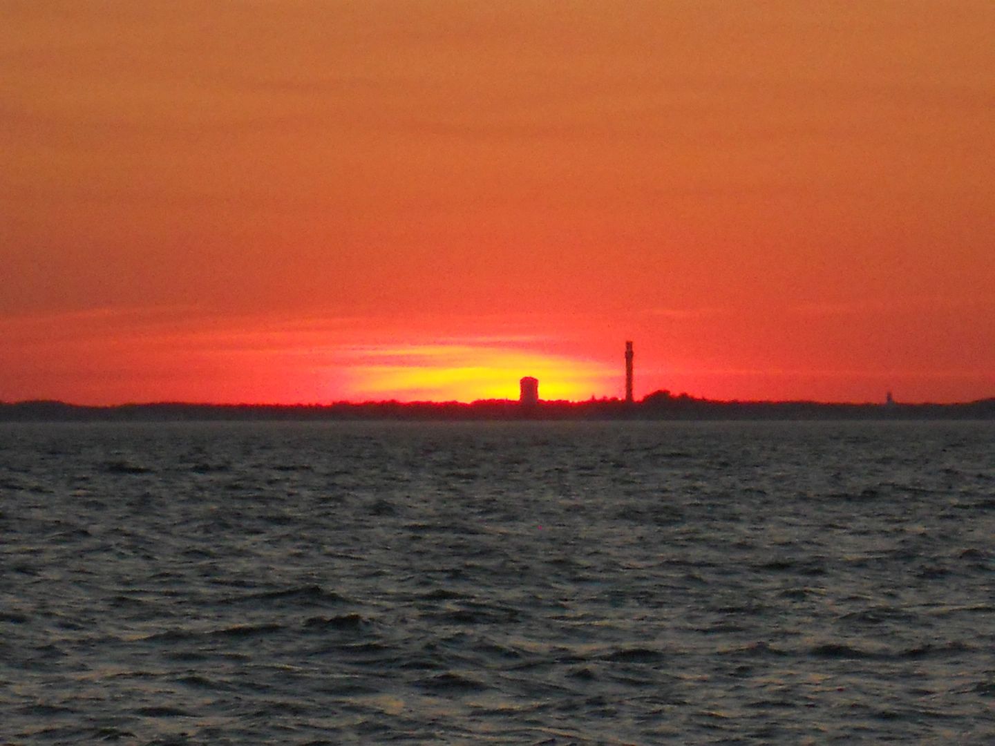 Sunset over a body of water with silhouetted towers on the horizon.