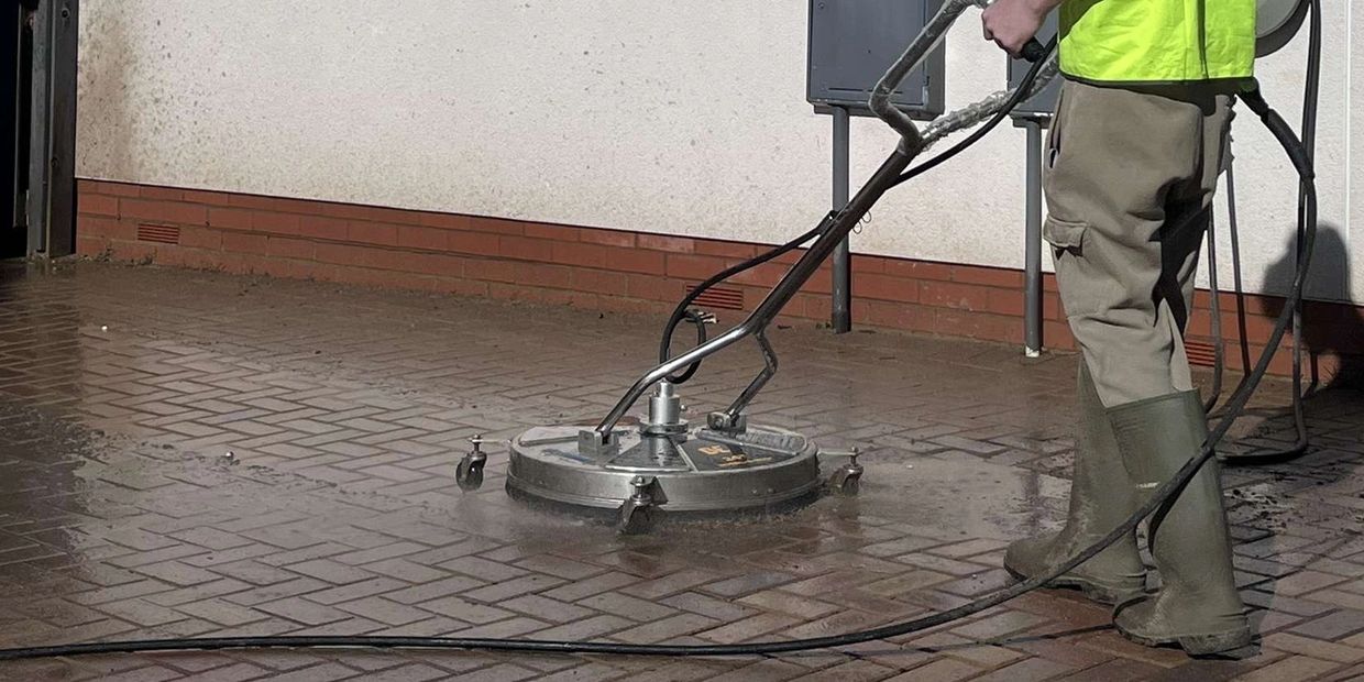 Person pressure washing a tiled floor outdoors.