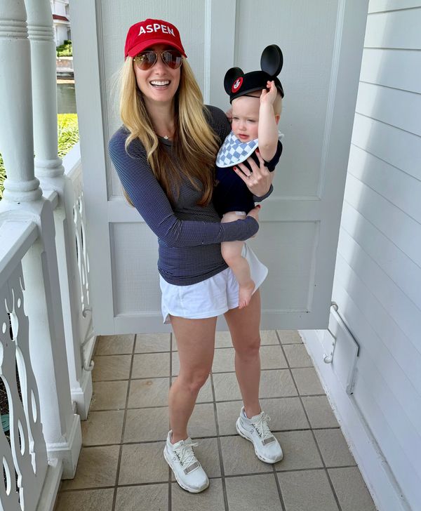 A woman holding a baby wearing Mickey Mouse ears on a porch.