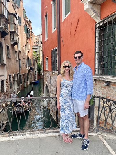 Couple posing by a canal in Venice with gondolas in the background.