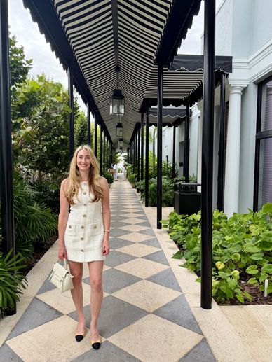 A woman in a white dress stands on a patterned walkway under a striped canopy.