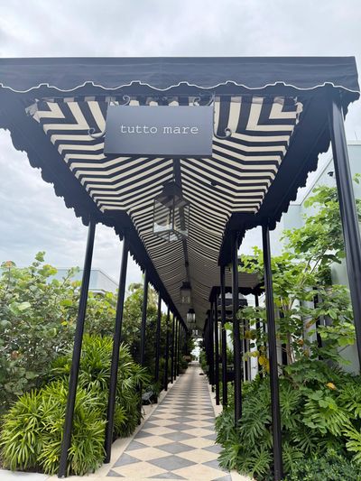 Striped black-and-white canopy walkway with greenery on sides and a sign reading 'tutto mare'.