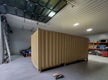 A large beige shipping container inside a spacious garage with shelves and tools.
