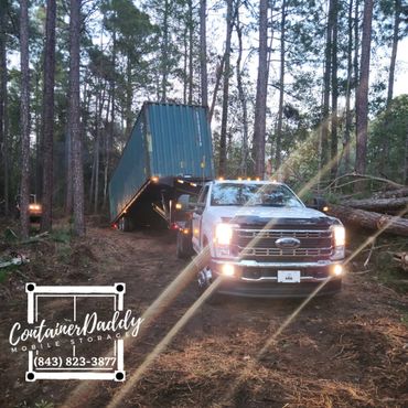 White Ford truck unloading a container in a forested area.