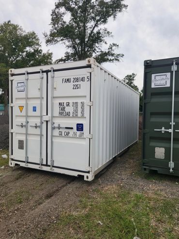 White shipping container parked on grassy ground beside a green container.