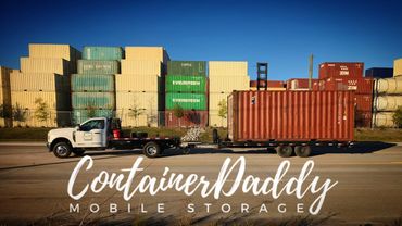 Truck with trailer carrying a red container in front of stacked shipping containers.