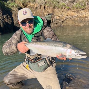 Man kneeling in water holding a large fish with a net nearby.