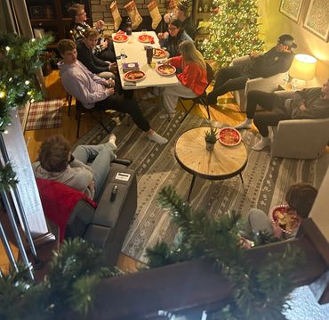 Group of friends enjoying a cozy Christmas gathering indoors with festive decorations and food.