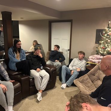 Group of young people sitting and chatting in a cozy living room with a decorated Christmas tree.