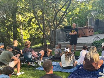 Outdoor group meeting with a speaker addressing attendees on a lawn.