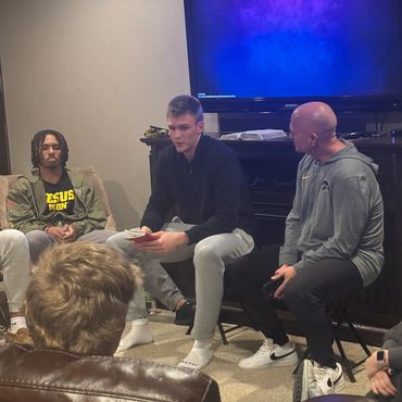 Group of people engaged in a discussion in a cozy room with a TV and books.