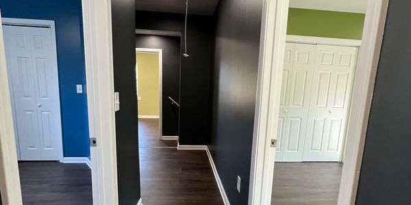 Hallway with dark walls and doors leading to colorful rooms.
