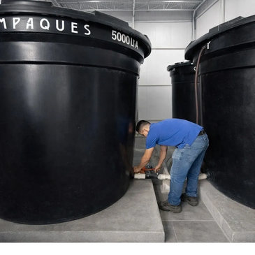 A man inspects large black water tanks labeled 5000 L in an indoor facility.