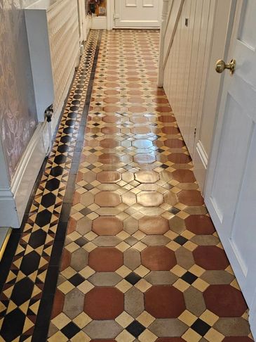 A hallway with vintage patterned floor tiles and a white door at the end.
