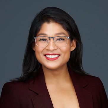 Smiling woman wearing glasses and a burgundy blazer.