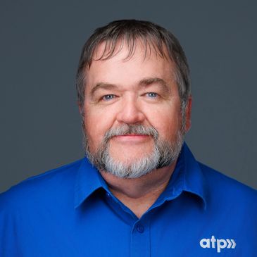Portrait of a middle-aged man with a beard wearing a blue shirt with an 'atp' logo.