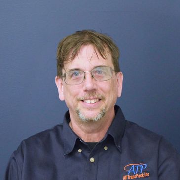 Man with glasses smiling wearing a dark shirt with company logo.