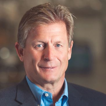 Professional headshot of a middle-aged man in a blue shirt and dark blazer.