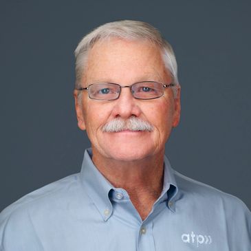 Smiling elderly man with glasses and mustache wearing a blue shirt.