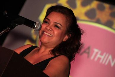 Woman smiling warmly while speaking at a microphone on stage.