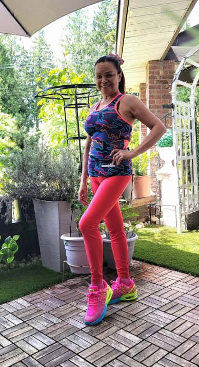 Woman in colorful workout clothes posing outdoors on a patio.